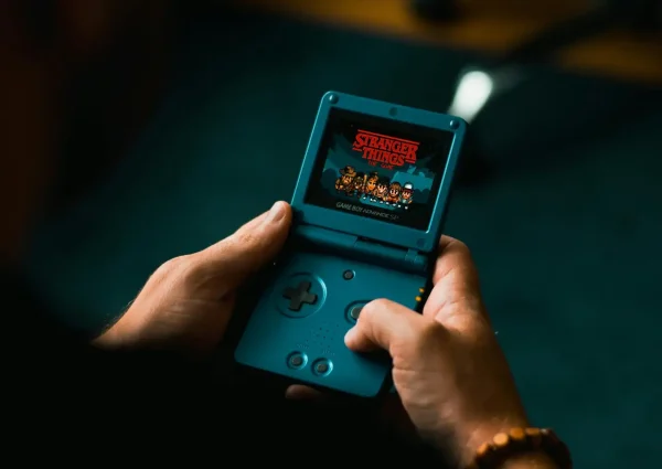 Close-up of individual holding a retro handheld gaming device, playing a classic video game indoors.